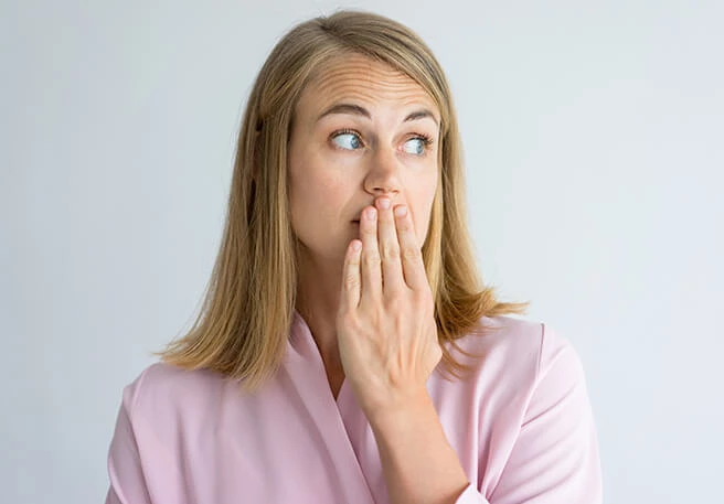 Frau hält Hand vor den Mund Knoblauchartiger Mundgeruch als Selen-Nebenwirkunge